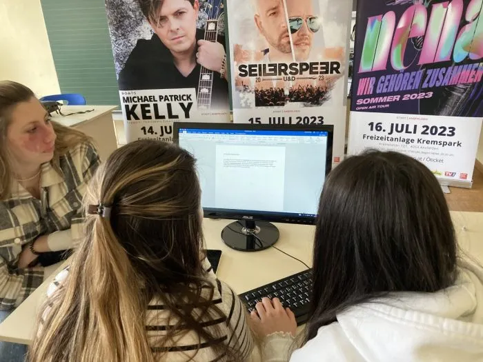 Schülerinnen schreiben am Computer einen Pressetext, dahinter Konzertplakate