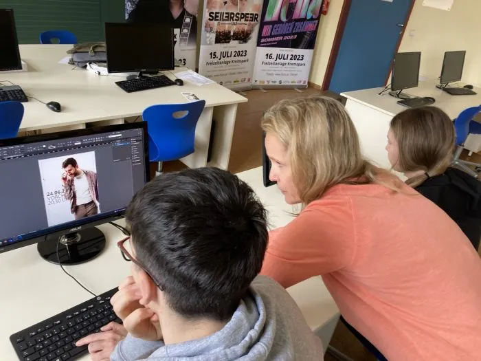 Ein Schüler gestaltet mit einer Lehrerin ein Plakat am Computer