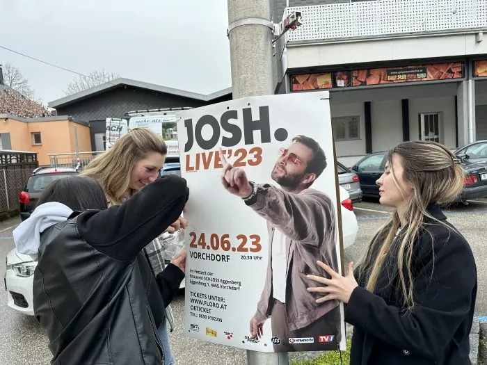 Schülerinnen hängen ein Plakat für das Konzert „Josh. Live ’23“ auf