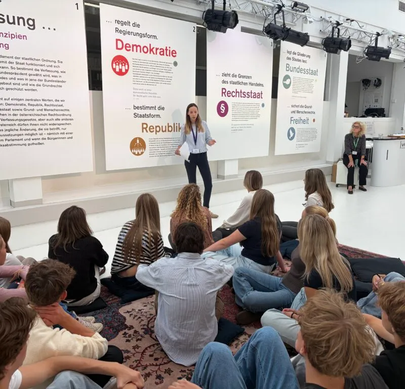 Schülerinnen und Schüler sitzen am Boden vor Schautafeln zu den Grundprinzipien der Verfassung