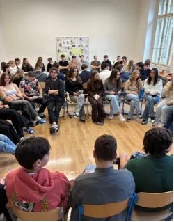 Schülerinnen und Schüler sitzen im Sesselkreis in einem Klassenraum