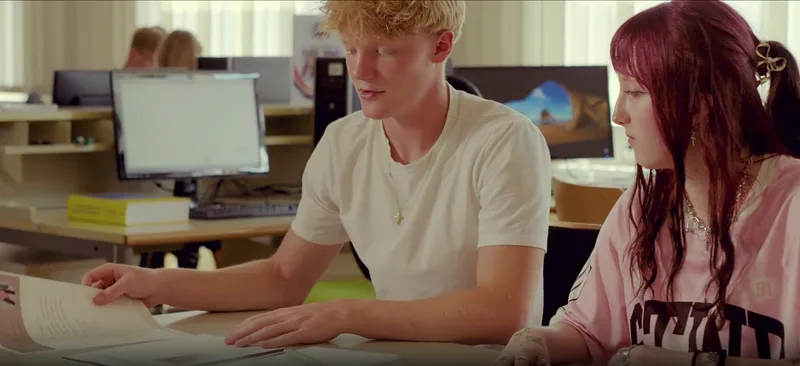 Ein Schüler und eine Schülerin arbeiten gemeinsam an Unterlagen am Computerarbeitsplatz