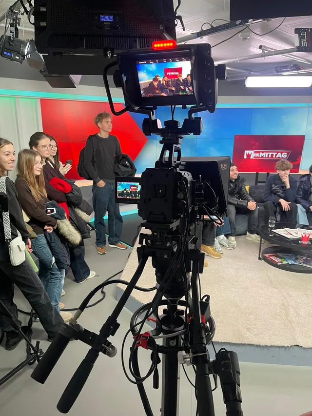 Schülerinnen und Schüler im Fernsehstudio, vorne eine Studiokamera